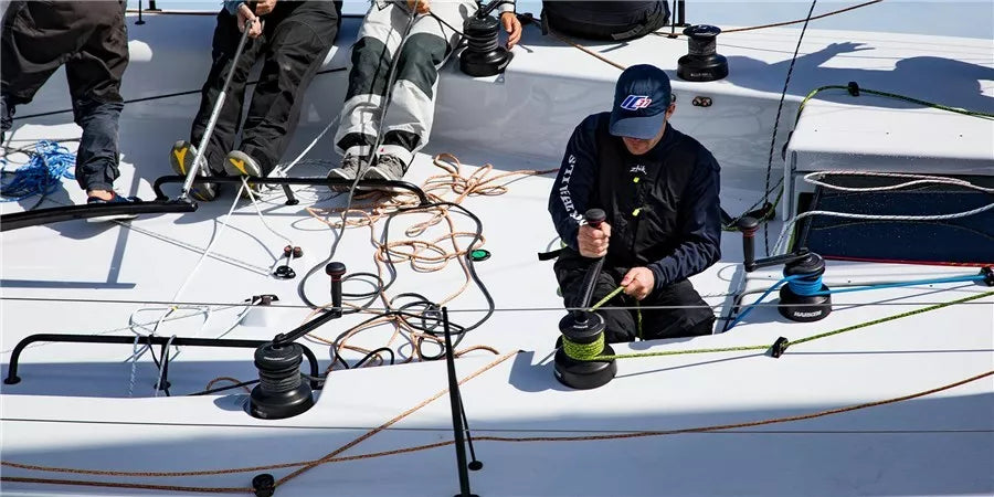 Crew operating sailing winches on a racing yacht deck with ropes and sailing gear